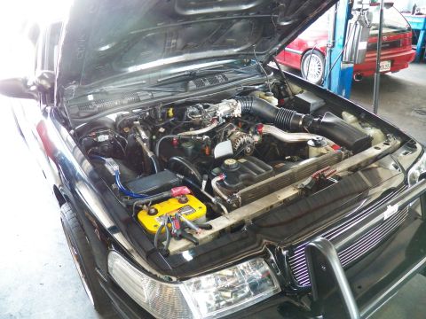 2003 Ford Crown Victoria - Open engine compartment of a black sedan showing air intake tube, alternator and yellow battery box.