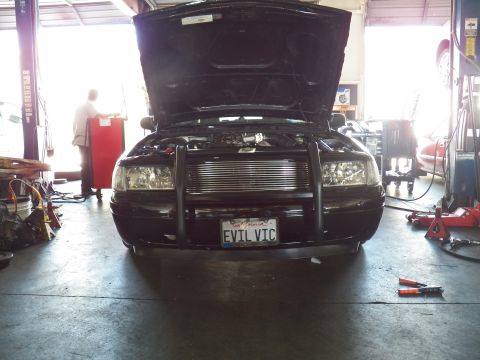 2003 Ford Crown Victoria - Black Crown Victoria sits hood-up in a garage, brush guard and EVIL VIC plate facing camera.