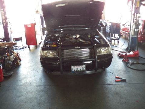 2003 Ford Crown Victoria - Wide front view of a black sedan with brush guard parked in a busy automotive shop.