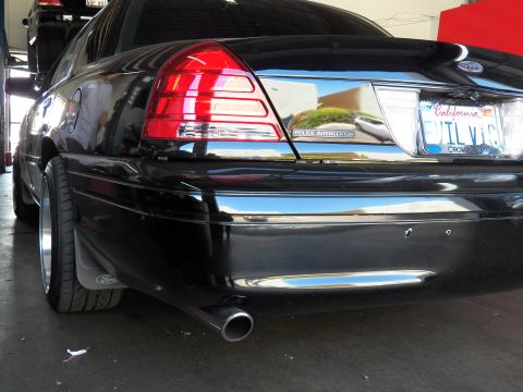 2003 Ford Crown Victoria - Rear corner of a black sedan with Police Interceptor badge, single exhaust tip and polished alloy wheel.