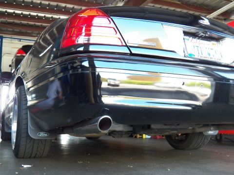 2003 Ford Crown Victoria - Ground-level rear quarter shot showing a chrome exhaust tip, taillight and Ford-branded mudflap.