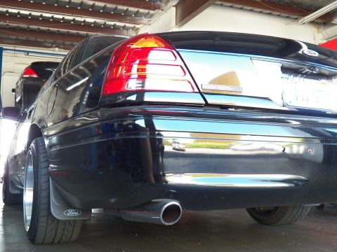 2003 Ford Crown Victoria - Black sedan rear quarter with polished exhaust tip, taillight detail and a dark machined-lip wheel.