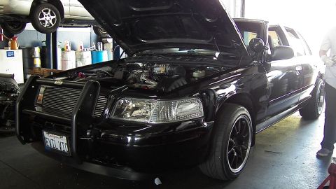 2003 Ford Crown Victoria - Black sedan front corner showing brush guard, billet grille, black alloy wheel and open hood.