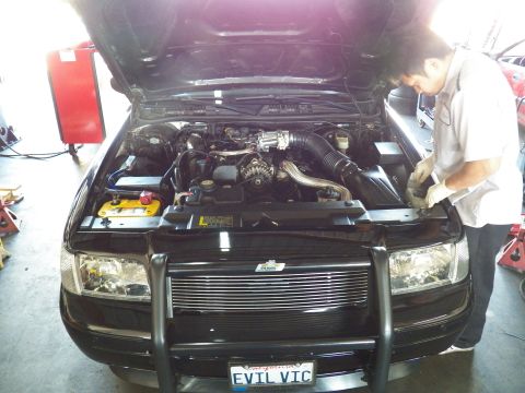 2003 Ford Crown Victoria - Open engine bay reveals a supercharger setup as a technician works; EVIL VIC plate sits below grille.