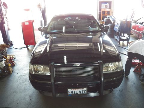 2003 Ford Crown Victoria - Head-on front view of a black sedan with brush guard and billet grille parked in a repair shop.