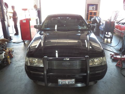 2003 Ford Crown Victoria - Front of a black Crown Victoria with brush guard as a worker stands at a station in the garage.