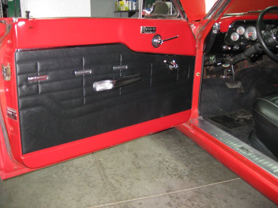 Interior shot of a red car showing the black door panel, chrome trim, and part of the dashboard with gauges
