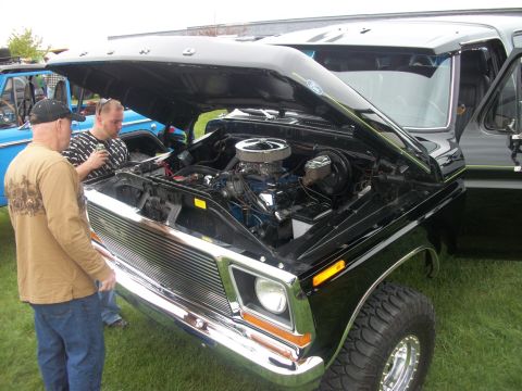 1996 Ford Bronco - A detailed look at the engine compartment of a classic Ford truck, with two onlookers examining the mechanics.