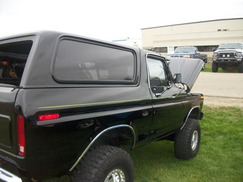 1996 Ford Bronco - A black Ford Bronco with its hood up is parked on grass, with other trucks in the background.
