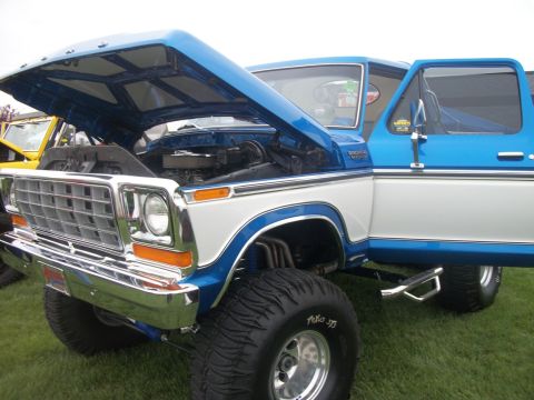 1996 Ford Bronco - This lifted pickup truck features a two-tone blue and white paint scheme with the hood and driver's door open, revealing the engine bay.