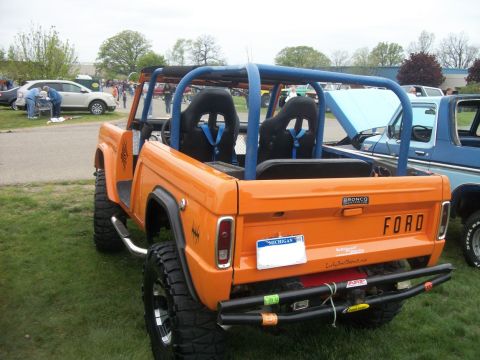 1996 Ford Bronco - This modified Ford Bronco features a custom roll cage and racing seats, parked next to a blue Ford pickup truck.
