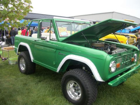 1996 Ford Bronco - A green Ford Bronco is displayed with its hood open, parked on grass next to other vehicles.