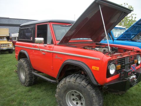 1996 Ford Bronco - This red Ford Bronco has its hood open, showing the engine bay. Another vehicle is parked behind it.