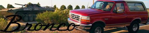 Red Ford Bronco with a tan top parked next to a military tank with 'DAKLEY' written on it
