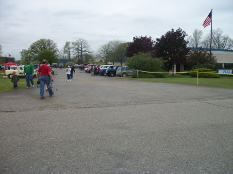 1996 Ford Bronco - An outdoor gathering of vehicles and people under a cloudy sky, with a building and flag in the background.