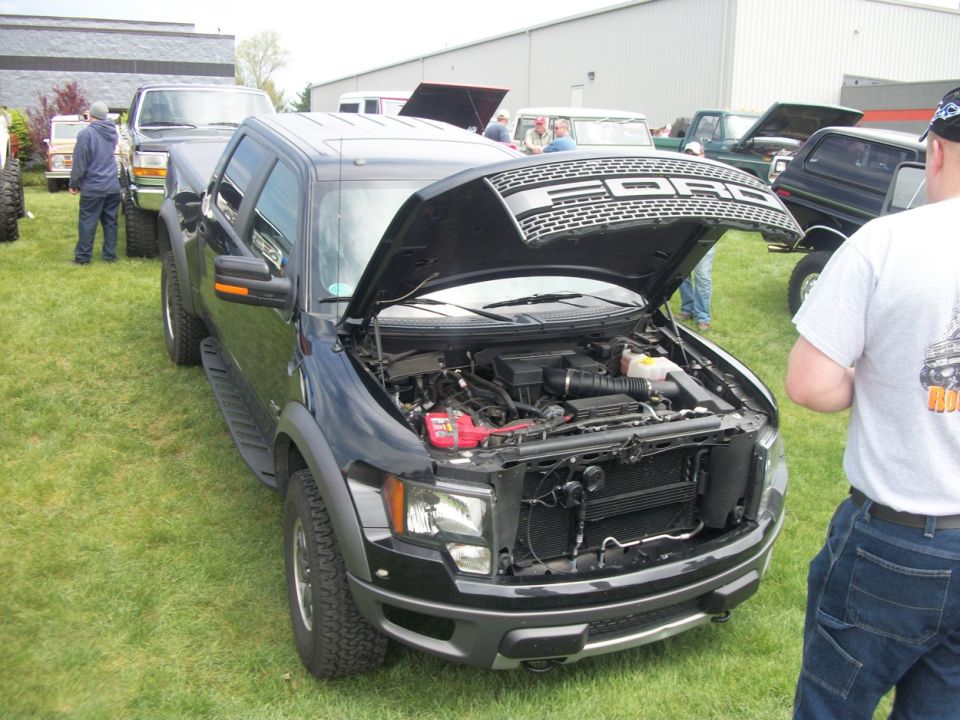 Black Ford pickup truck, hood open, showing engine. Front view, parked on grass