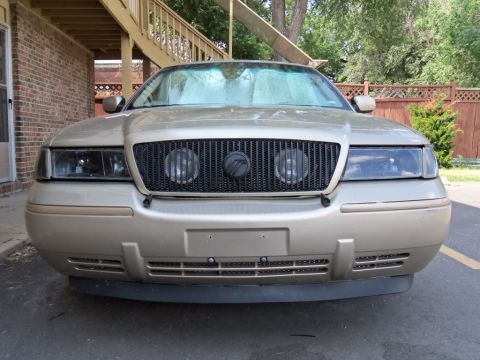 2000 Mercury Grand Marquis - The front of a gold Mercury Grand Marquis is shown, a black grille and sunshade on the windshield.