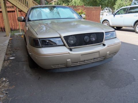 2000 Mercury Grand Marquis - A gold 2000 Mercury Grand Marquis is parked in front of a wooden fence and a white SUV.