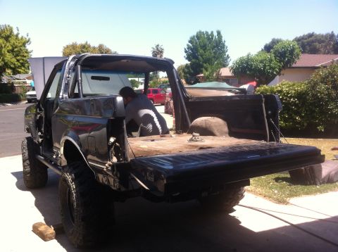 1989 Ford Bronco - A person works on the interior of a black Ford Bronco with its roof removed and tailgate down.