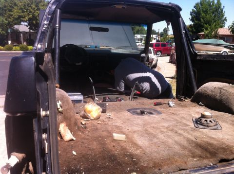 1989 Ford Bronco - The interior of a 1989 Ford Bronco is shown with the carpet removed as a person works on the floor.