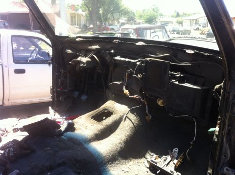1989 Ford Bronco - The interior of a vehicle is shown with the dashboard and carpet removed, exposing wires and components.