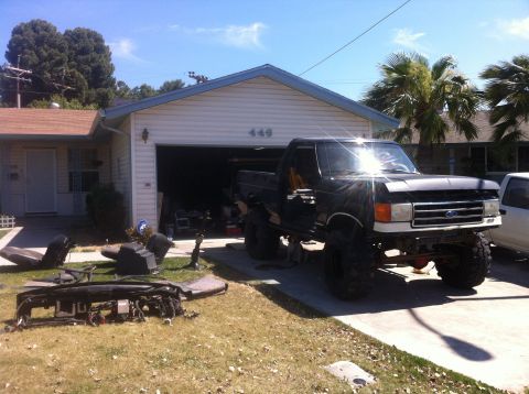 1989 Ford Bronco - A black lifted Ford F-Series truck sits in a driveway with its front end disassembled, suggesting ongoing repairs or modifications.