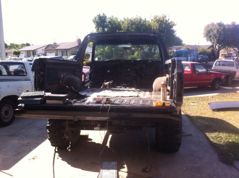 1989 Ford Bronco - The rear of a black pickup truck is shown with the bed stripped down, revealing the frame and suspension components.