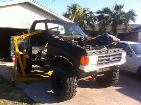 1989 Ford Bronco - Ford truck body being worked on with a yellow engine hoist in a driveway.