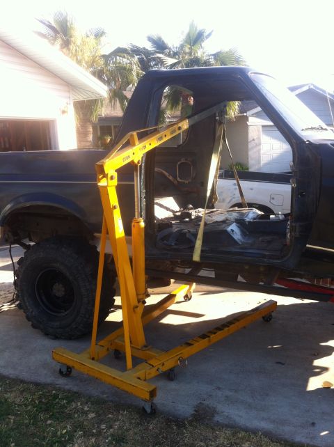 1989 Ford Bronco - A Ford Bronco body is undergoing work with an engine hoist attached, doors removed, and interior exposed.
