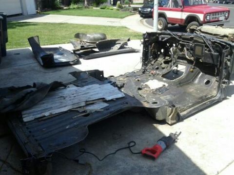 1989 Ford Bronco - A disassembled vehicle chassis and floor pan lie on the ground, with a red and white Ford Bronco visible in the background.