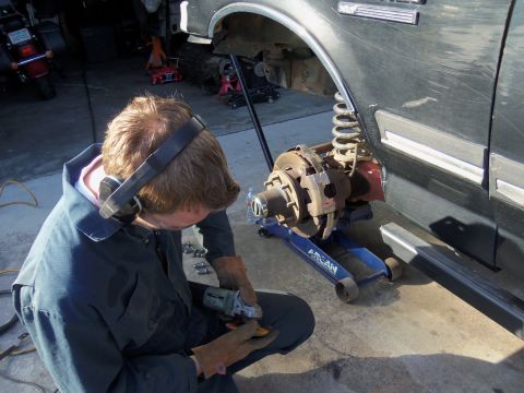 1968 Ford Bronco - A mechanic works on the brake assembly of a vehicle, which is elevated on a jack.