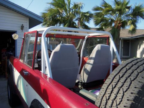 1968 Ford Bronco - Interior view of a red and white 1968 Ford Bronco with a white roll cage and grey seat covers.