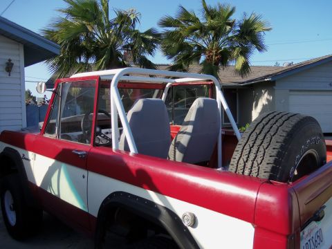 1968 Ford Bronco - A red and white Ford Bronco is parked in a driveway with palm trees and a house in the background.