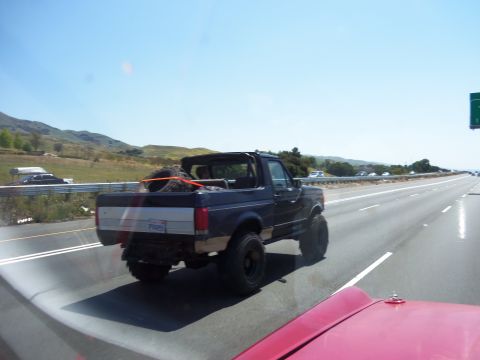 1968 Ford Bronco - A dark blue SUV with a spare tire secured in its bed drives down a highway.
