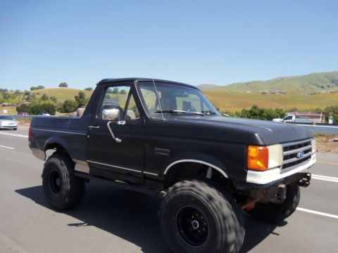 1968 Ford Bronco - Lifted black Ford Bronco with aftermarket wheels and tires on a highway.
