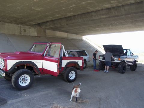 1968 Ford Bronco - A red and white 1968 Ford Bronco is parked next to a dark Ford truck under a concrete overpass.