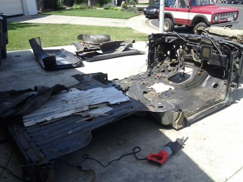 1968 Ford Bronco - The chassis of a 1968 Ford Bronco is disassembled on a driveway, with a reciprocating saw on the ground.