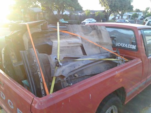 1968 Ford Bronco - Pickup truck bed filled with various car parts, strapped down for transport.