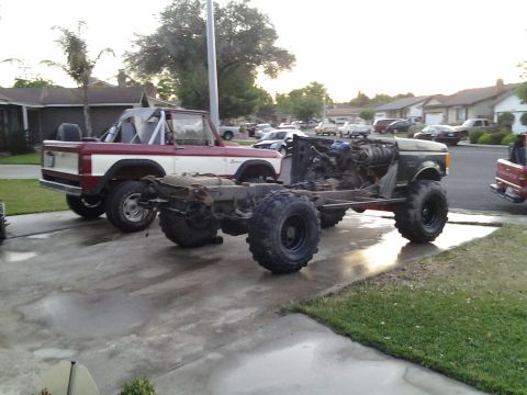 1968 Ford Bronco - A disassembled Ford Bronco sits on its chassis next to a complete Bronco, with other vehicles in the background.