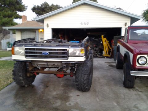 1968 Ford Bronco - A lifted 1987 Ford F-Series truck is parked in front of a garage, with a red Bronco to its right.