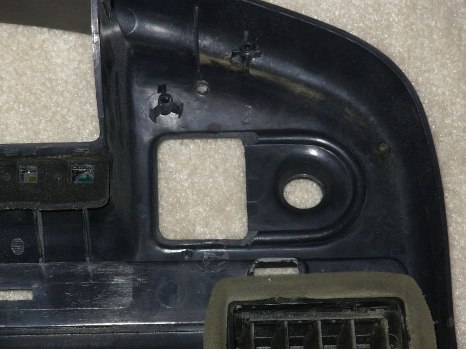 Black plastic dashboard bezel trim with vent grille and mounting holes on white surface