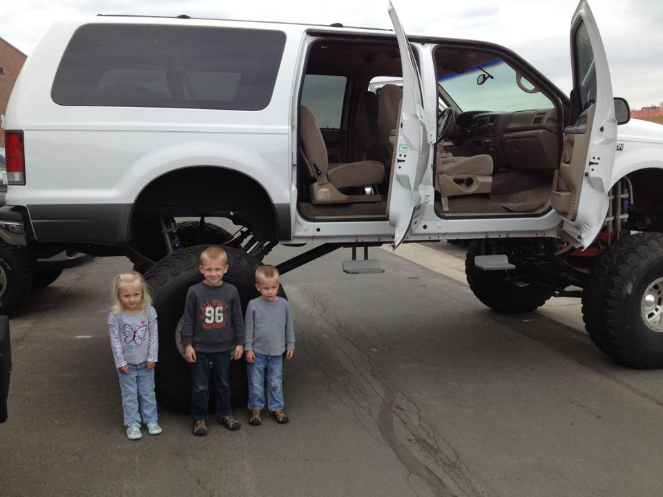 Lifted 2001 Ford Excursion with doors open, three children standing next to it