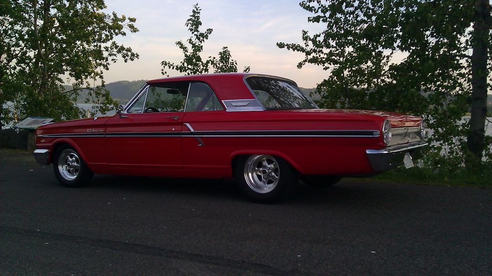 Red 1964 Ford Fairlane coupe with chrome trim and aftermarket wheels parked on asphalt