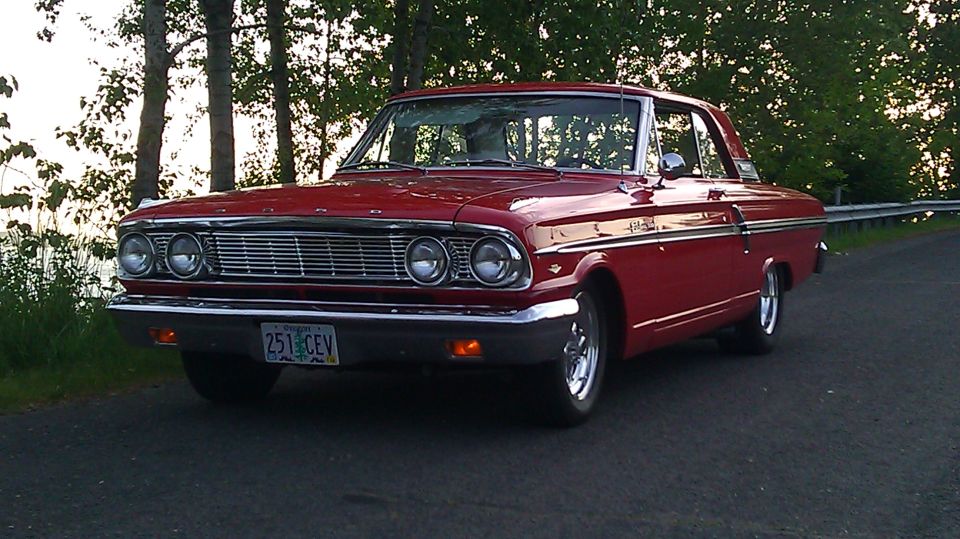 Red 1964 Ford Fairlane parked on a road with trees in the background