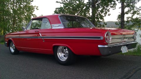 1964 Ford Fairlane - A red 1964 Ford Fairlane coupe is viewed from the rear quarter angle, parked beside a body of water.
