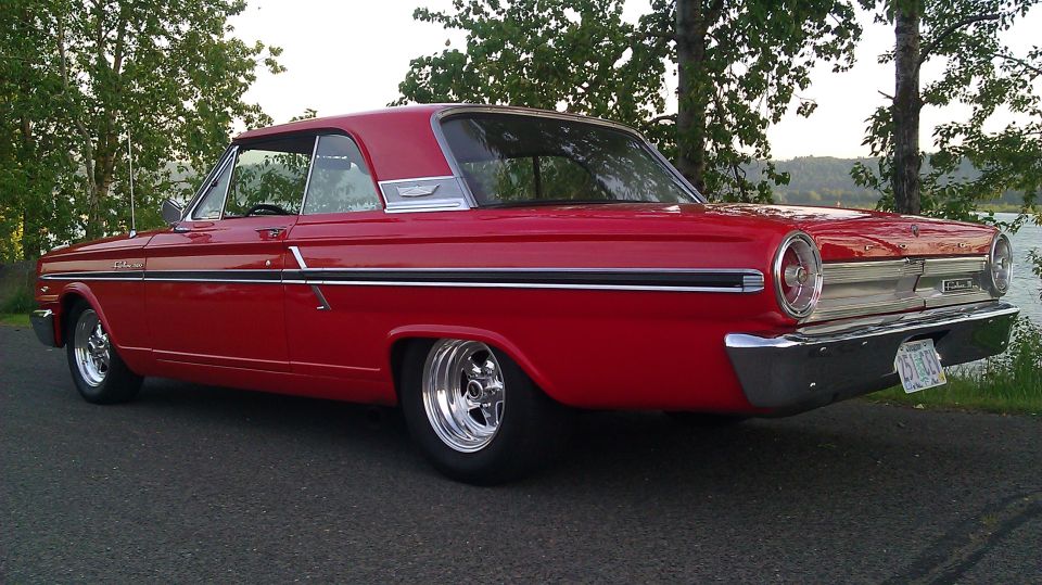 Red 1964 Ford Fairlane coupe, rear quarter view, lowered stance, chrome wheels, parked roadside