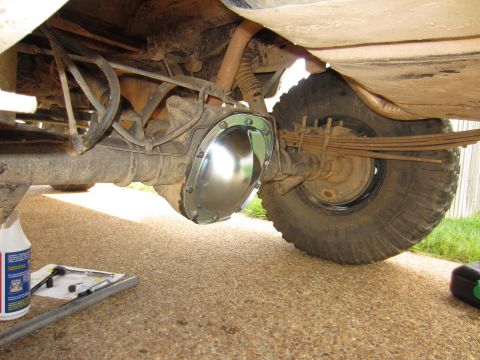 1992 Ford Bronco - A shiny aftermarket differential cover is installed on the rear axle of a vehicle, with tools and a bottle of fluid nearby.