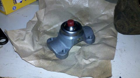 1978 Ford Bronco - A brake master cylinder part is shown on brown paper, with a red cap on top and mounting holes on the base.