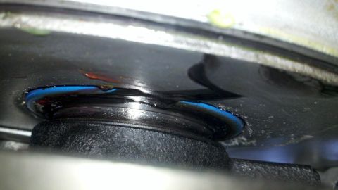 1978 Ford Bronco - This image shows a close-up view of a leaking engine oil seal, with blue sealant and oil pooling around it.