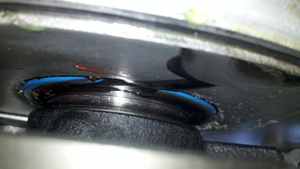 Close-up of a leaking engine oil seal with blue sealant and oil visible